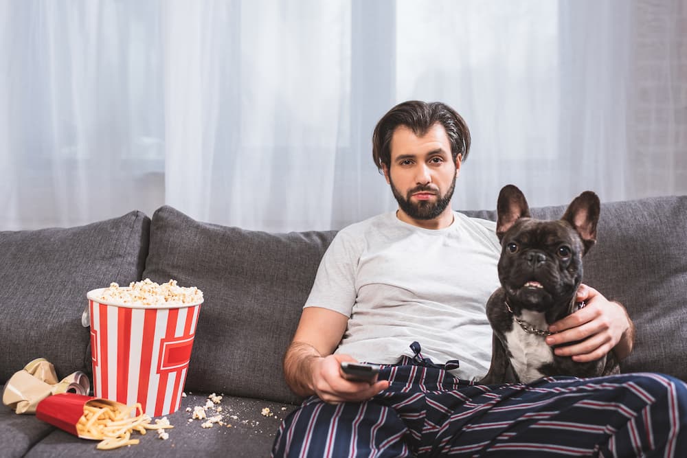Imagem mostra um homem com um cachorro em cima de um sofá sujo