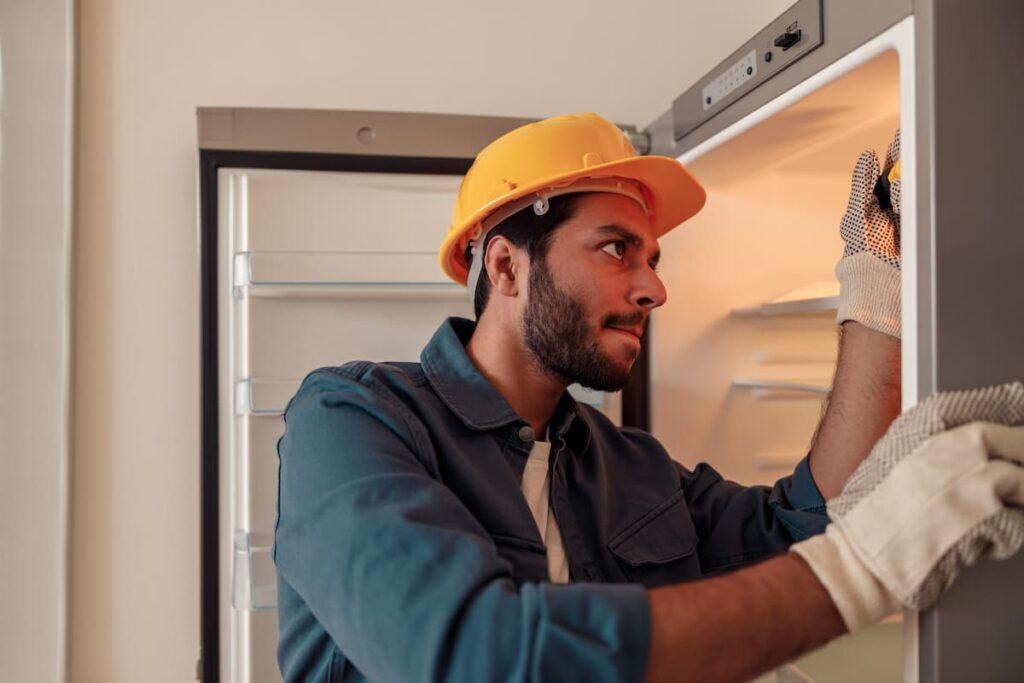 Imagem mostra técnico reparando geladeira barata usada.